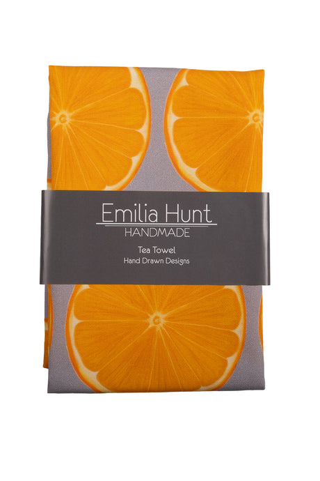 Folded tea towel with orange slice design on a grey background with card band across centre showing Emilia Hunt Handmade logo